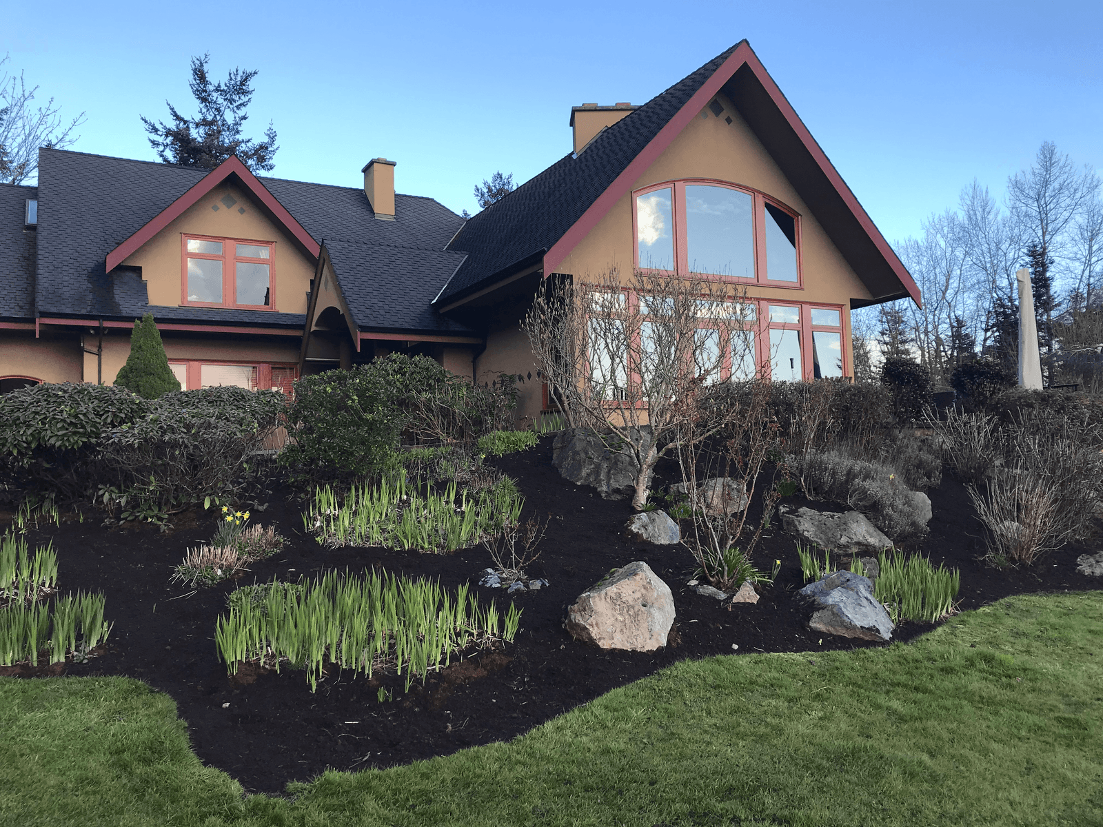 The same hillside property after restoration — clean mulched beds, fresh plantings, rock features and a tidy lawn